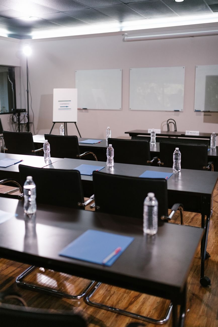 A neatly arranged conference room with tables, chairs, water bottles, and stationery ready for a meeting.